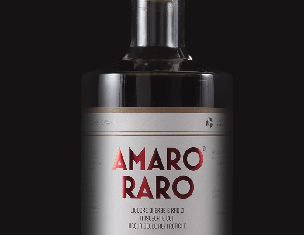 Dettaglio bottiglia di Amaro Raro da 70cl, liquore artigianale italiano con erbe aromatiche e acqua delle Alpi Retiche, su sfondo nero.